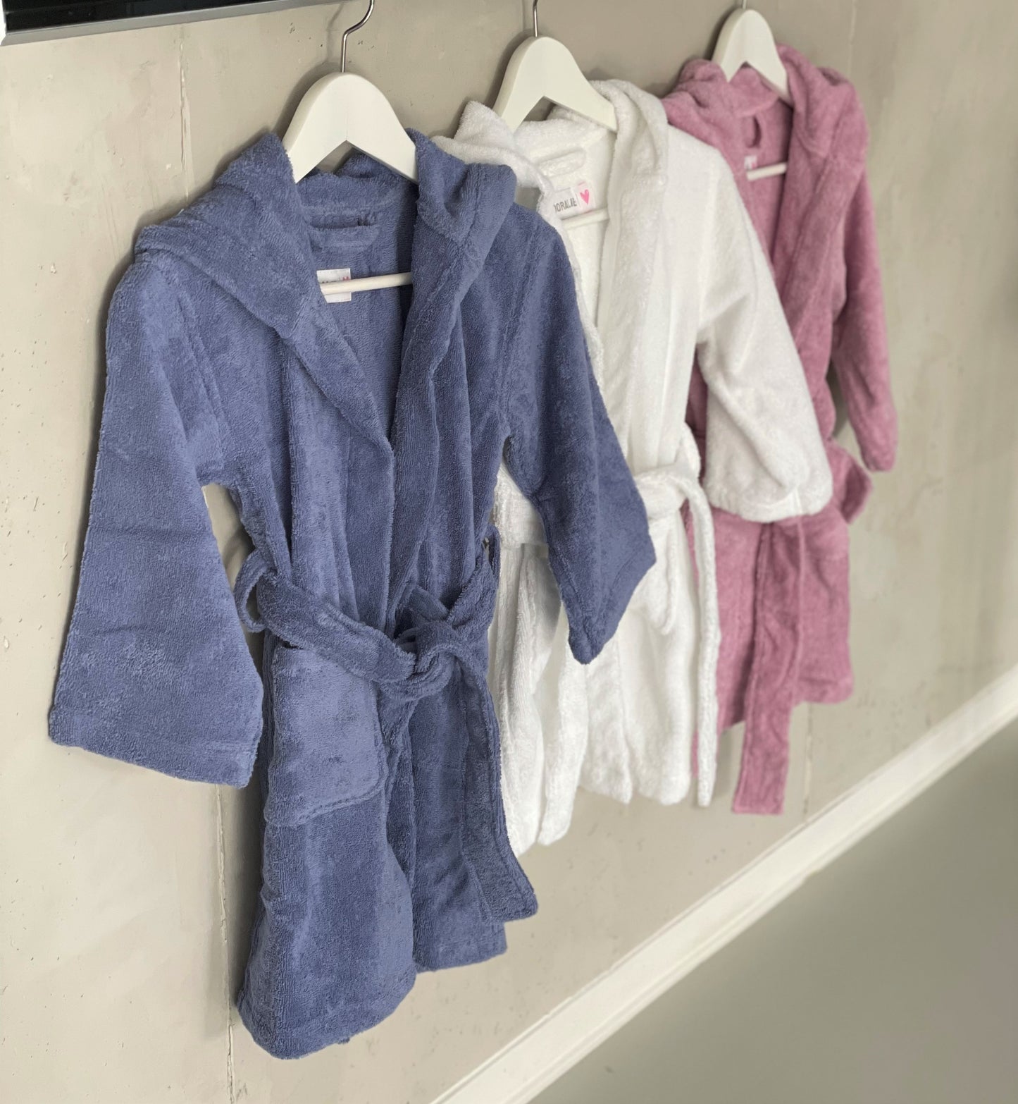 Bademantel für Kinder 3-6 Jahre aus Baumwolle in den Farben blau, rosa und weiß. Die Bademäntel haben zwei Taschen und eine Kapuze.