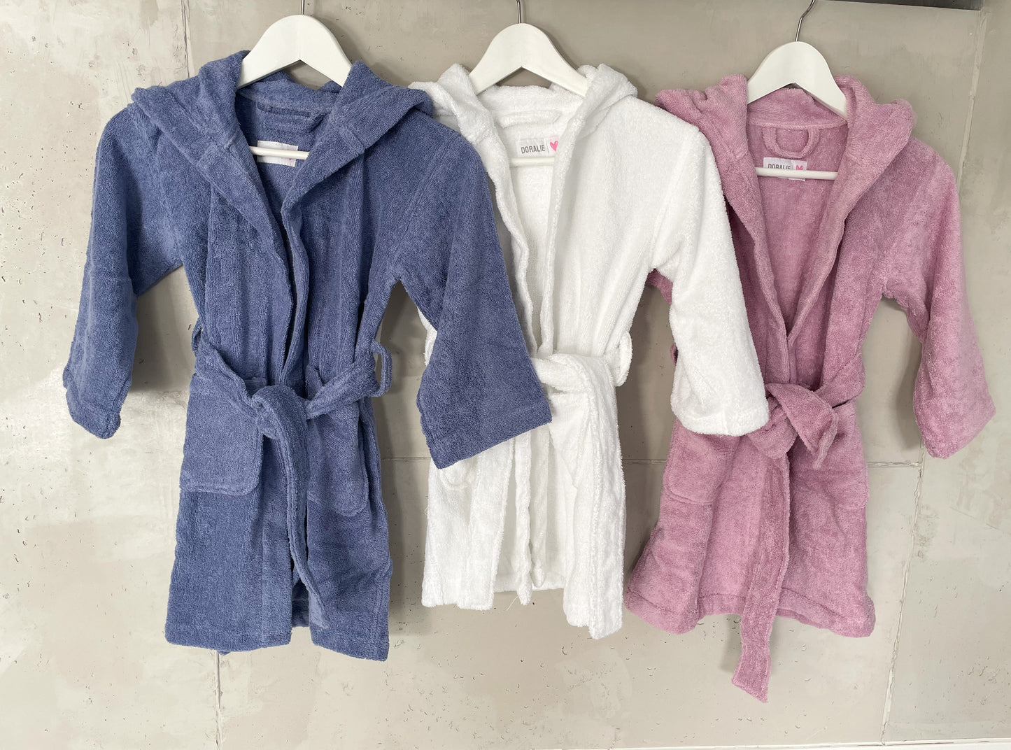 Bademantel für Kinder 3-6 Jahre aus Baumwolle in den Farben blau, rosa und weiß. Die Bademäntel haben zwei Taschen und eine Kapuze.